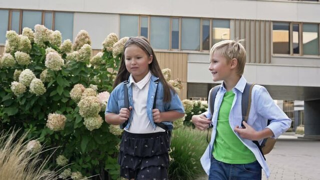 Two little classmates, a boy and a girl, are walking around the school yard in a good mood. School friendship.
