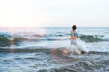 Swimming, traveling, playing with water. Girl in a swimsuit is playing on the beach with a sea wave - jumping, running, having fun.