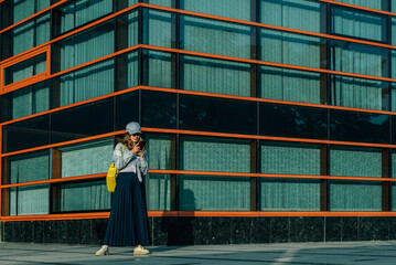 portrait of a woman in the summer on the street against the background of the glass facade of a modern building on a city street with a phone in her hands