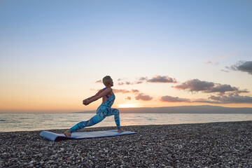 Young woman practicing yoga on the beach at sunrise. Harmony, wellbeing, meditation, healthy...
