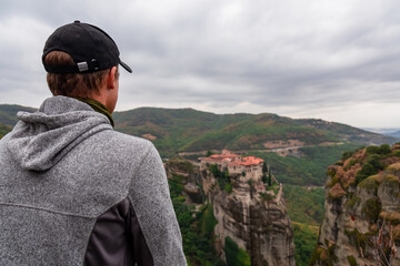 Selected focus on man with panoramic view of Holy Monastery of Varlaam, Kalambaka, Meteora, Thessaly, Greece, Europe. Rock formations overgrown with moss creating moody vibes. UNESCO World Heritage
