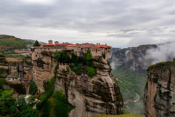Fototapeta premium Scenic view of Holy Monastery of Varlaam on cloudy foggy day, Kalambaka, Meteora, Thessaly, Greece, Europe. Rock formations overgrown with green moss creating moody atmosphere. UNESCO World Heritage