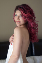 Topless redhead woman covering her breasts with a white bed shet 