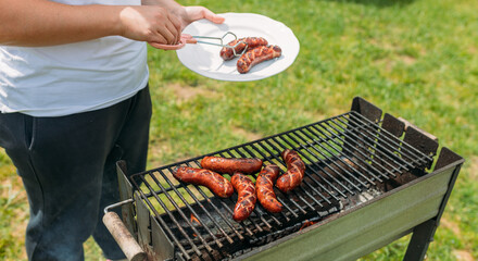 Grilled pork sausage on a cast iron grill. Hand of young woman grilling some meat. Young female...