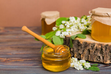 Sweet honey jar surrounded spring acacia blossoms. Honey flows from a spoon in a jar. jars of clear fresh acacia honey on wooden background