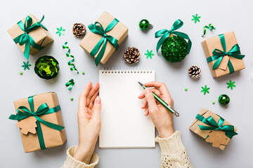 Woman writing Christmas to do list on notebook on colored background with xmas decorations