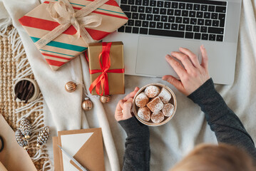 Top view of a woman drinking cocoa with marshmallows and searching the internet for new year gifts.