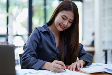 A portrait of an Asian female accountant with a smiling face sits and uses a calculator to calculate taxes for companies to submit evidence to the Revenue Department