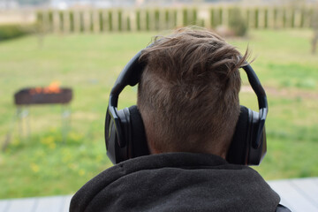 Young man enjoys listening music in headset from cell phone and resting outdoors. Back view.
