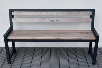 Metal wooden benche on grey terrace on light house wall background outdoors.
