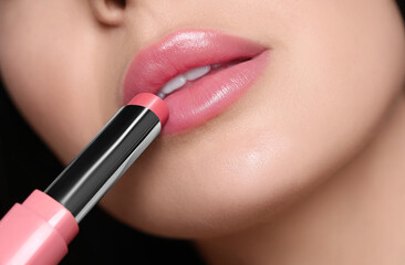 Naklejka premium Closeup view of young woman applying beautiful nude lipstick
