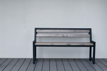 Metal wooden benche on grey terrace on light house wall background outdoors.
