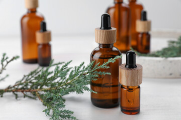 Bottles of juniper essential oil and fresh twig on white wooden table