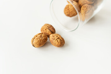 Beautiful whole walnut kernels in a glass jar, whole nuts in shell spilling on the table. Selective focus, noise.