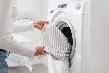 woman load dirty clothes in washing machine indoors