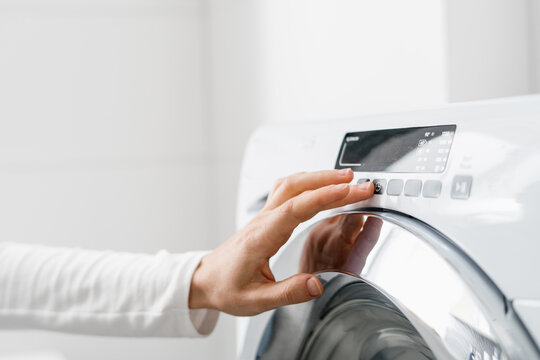 female hand press button on washing machine indoors