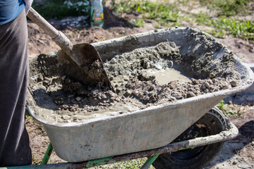 A worker kneads a mixture of concrete in a wheelbarrow at a construction site.