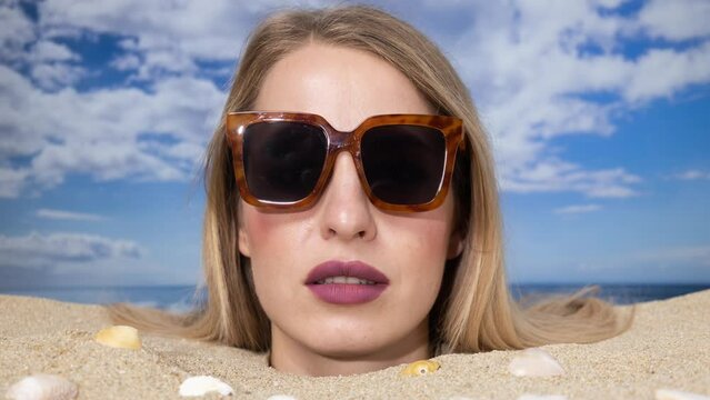 Woman buried in sand on beach with sunglasses