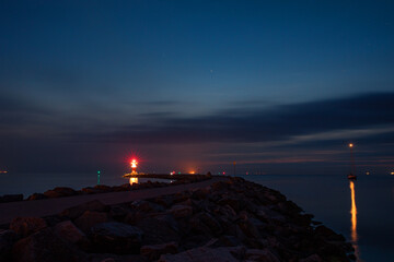 nachtszene am meer mit einem leuchtturm am ende des weges und weiteren Lichtern in der ferne
