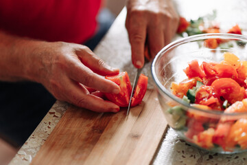 Close up on man slicing up small tomatoes. male hand cutting tomato on cutting board at home. cooking, food and home concept
