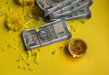 Plenty of Five Hundred Indian Rupee currency notes and traditional earthen Diwali lamp arranged with scattered marigold flowers. Hard currency is worshiped as Laxmi - a goddess of wealth. - obrazy, fototapety, plakaty