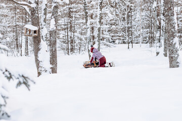 Fototapeta na wymiar Happy little African-American girl in red hat and jumpsuit rides on tubing in the winter park.Beautiful trees are covered with white snow.Winter fun,active lifestyle concept.Selective focus,copy space