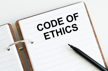 On a white background lies a notebook with words CODE OF ETHICS
