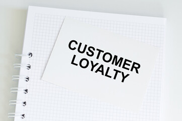 Customer Loyalty text on a card against the background of a blank notebook page on the table