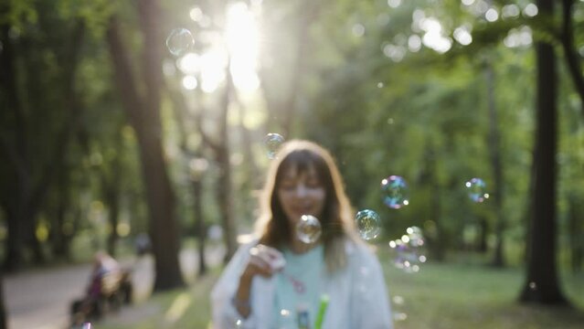 Girl inflates soap bubbles outdoor in park. Golden hour sunset light. Beautiful caucasian young girl.