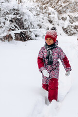 Fototapeta na wymiar Happy little African-American girl in a red hat and jumpsuit walks in the winter forest.Beautiful trees are covered with white snow.Winter fun,active lifestyle concept.