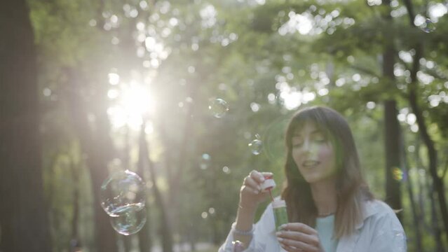 Girl inflates soap bubbles outdoor in park. Golden hour sunset light. Beautiful caucasian young girl.
