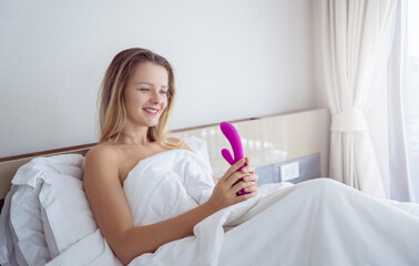 Young sexy woman in the bed holding in her hands a sex toy for adults - obrazy, fototapety, plakaty