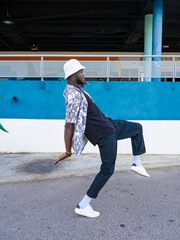 African American man doing strange poses in the street with blue and white wall background.