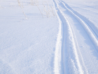 Track of traces from a snowmobile in drifts of white snow. Nature and outdoor on a winter sunny day. Background or backdrop