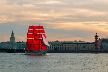 A boat with scarlet sails on water surface against a Saint Petersburg cityscape by summer day