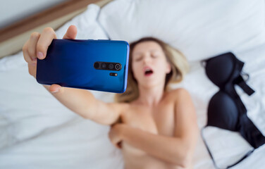 Young sexy woman posing in front of smartphone in his hand and working as webcam model