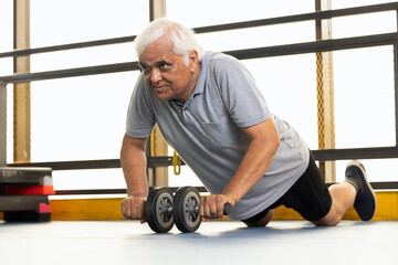 Active old man in sportswear using abdominal exercise roller for stretching forward
