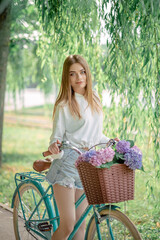 beautiful fair-haired girl on a bicycle with flowers. Hydrangeas.