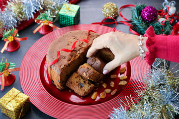 Woman serving homemade Christmas plum cake in red plate India Kerala. Fruitcake of dried fruit, nuts, spices , rum New Year party, Easter, Christmas Eve. Indian Christmas celebration - obrazy, fototapety, plakaty