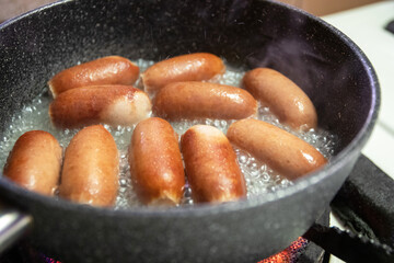 Sausages cooking with water on pan. Healthy and easy meal.