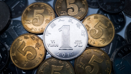 One Chinese yuan resting on several five jiao coins is shot close-up. Many coins in denominations of one Chinese yuan in the background. One yuan coin minted in 2017 - obrazy, fototapety, plakaty