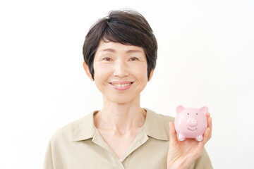 豚の貯金箱を持ってカメラ目線で笑顔の中年女性　白背景