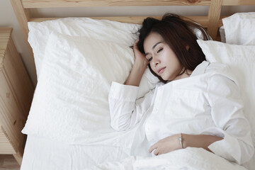 Young depressed asian woman lying and hugging pillow while crying on bed in hotel bedroom with low light environment. Sad girl, unhappy and loneliness concept.