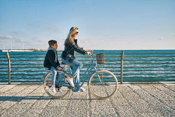 Happy family, Carefree mother and son with bike riding on beach having fun, on the seaside promenade on a summer day, enjoying vacation. Togetherness Friendly concept