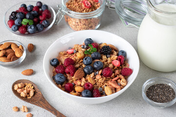 Crispy muesli with fresh berries, almonds in bowl and milk in jug, chia seeds for making pudding on light background. Healthy breakfast concept