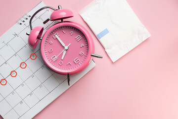 Women's menstruation Calendar, sanitary napkin in a package with pink alarm clock on a pink background. The concept of critical days time. - obrazy, fototapety, plakaty