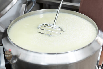 Making cheese from fresh milk at a private cheese factory. The process of mixing with a large whisk.