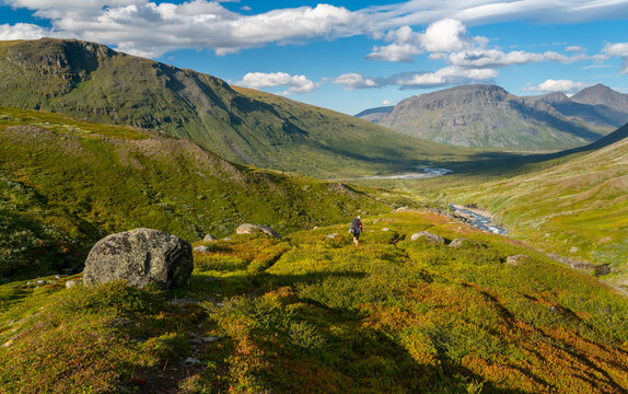 Female Hiker With Heavy Backpack And Gear Walking In Mountain Valley In Remote Arctic On Sunny Summer Day.Noajdevagge Valley With Laddebakte Mountain In The Back,Sarek National Park,Lapland,Sweden