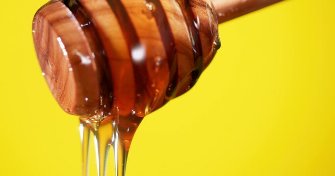 Natural honey on a wooden honey spoon on a yellow background.