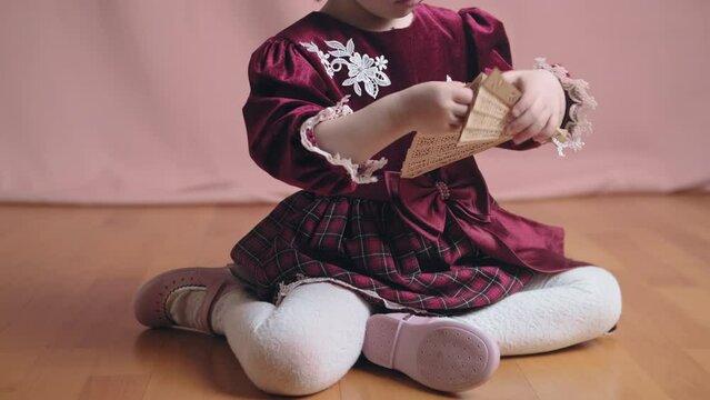 Cute little girl in an vintage burgundy dress is playing with a wooden fan. The concept of children theater productions and developing acting circles. Coral background